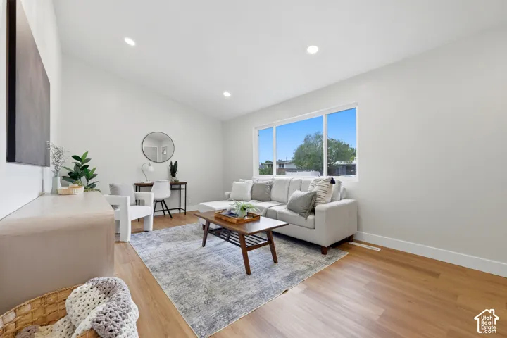Vaulted ceiling with recessed lighting, large multi-pane window, wood-finish flooring, and white painted walls