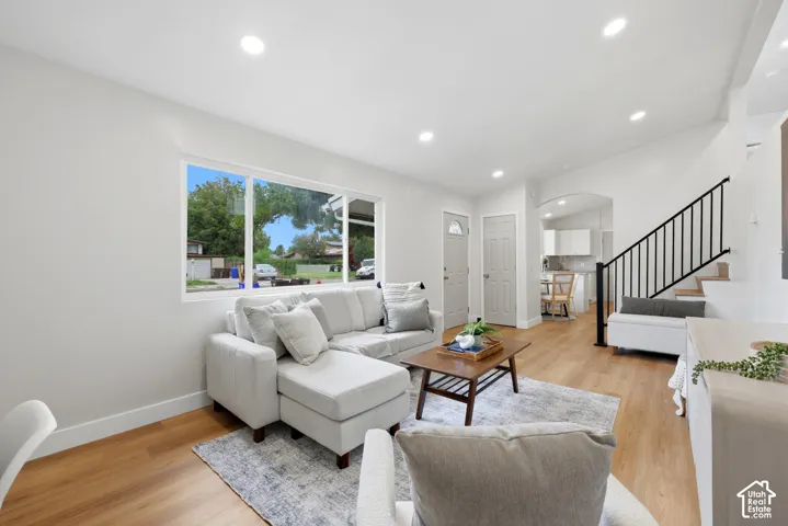 Recessed lighting, wood-finish flooring, white walls, arched doorway, and a staircase with black railing