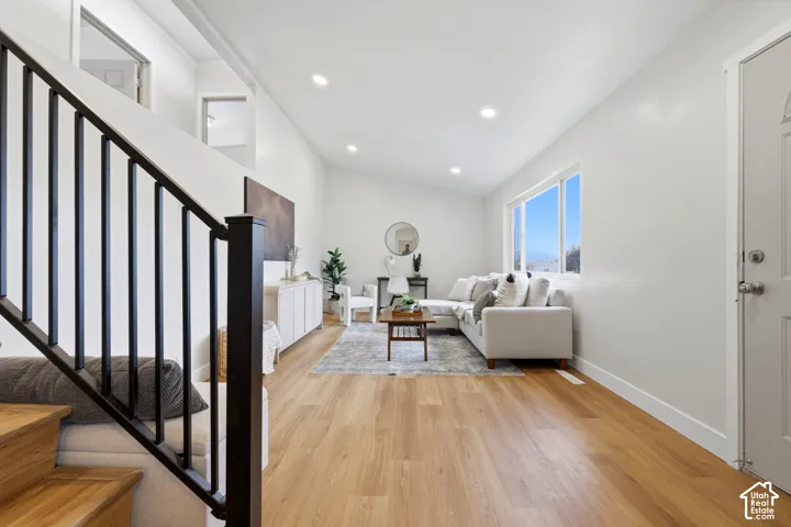 Light-filled living area featuring wood-finish flooring, recessed lighting, and a modern staircase with dark metal balusters