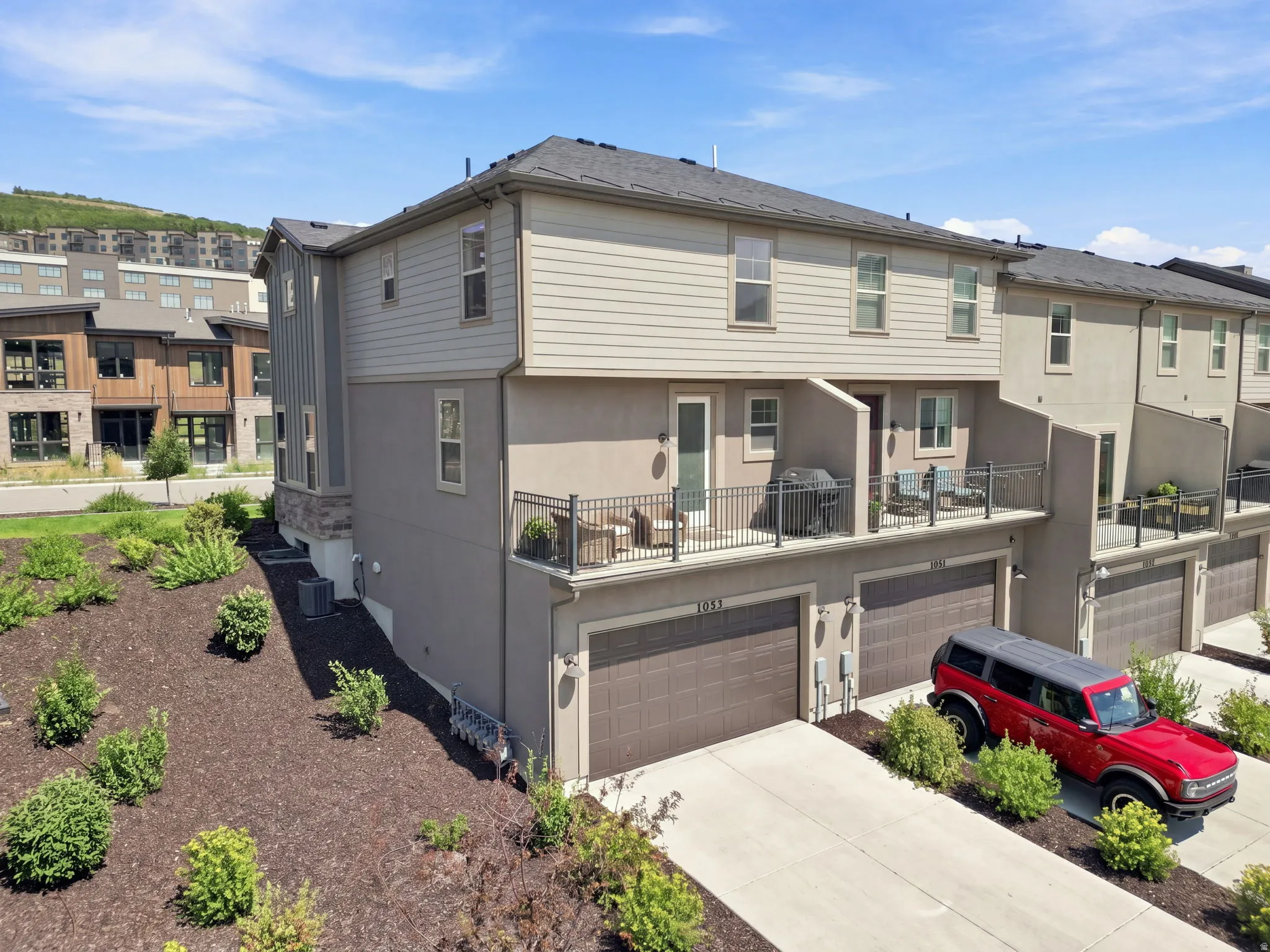 Multi-level townhouse with private balconies, attached garages, and a sloped, landscaped front yard