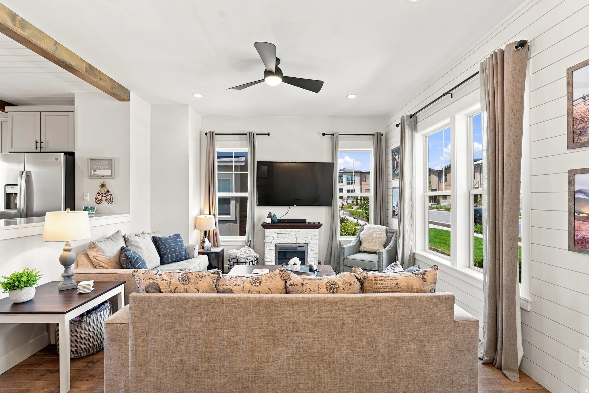 Open-concept living space featuring wood-finish flooring, a contemporary ceiling fan, and a fireplace with a white stone surround