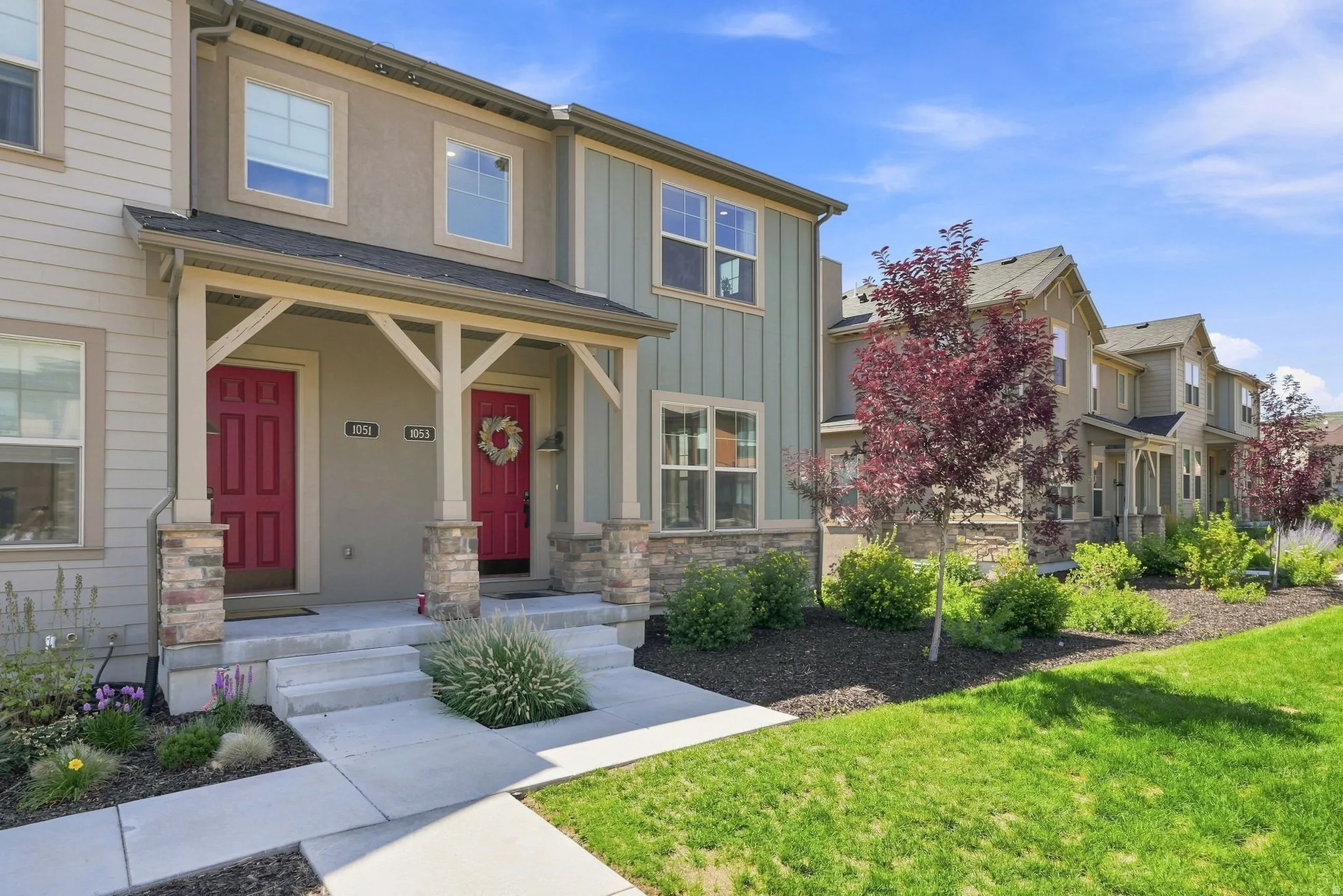 Multi-unit facade featuring dual red entry doors, stone and wood-clad columns, and a covered porch