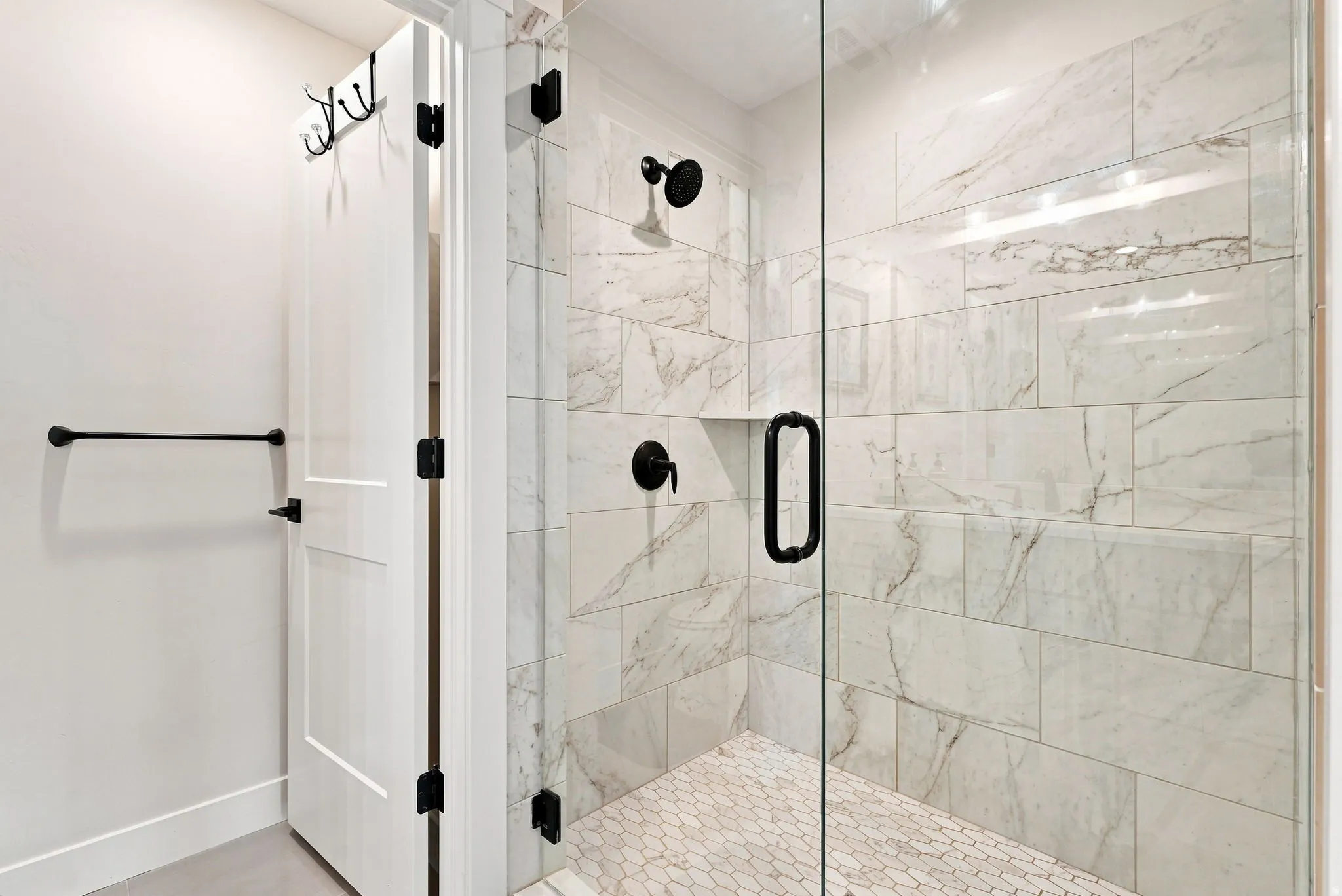 Walk-in shower with clear glass enclosure, large format wall tiles, hexagonal floor tiles, and matte black fixtures