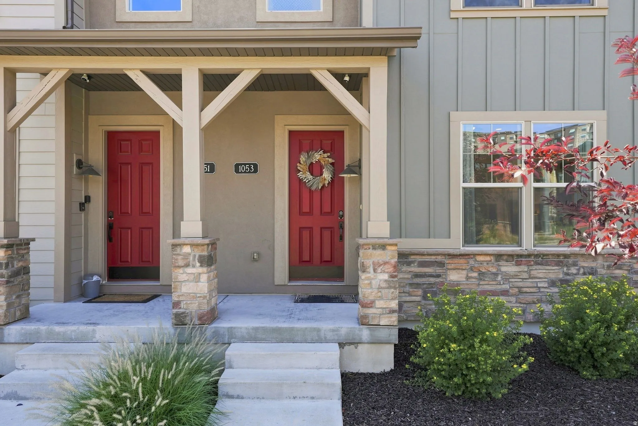Entryway with red paneled doors, covered porch, decorative wood beams, stone column bases, and a stone foundation
