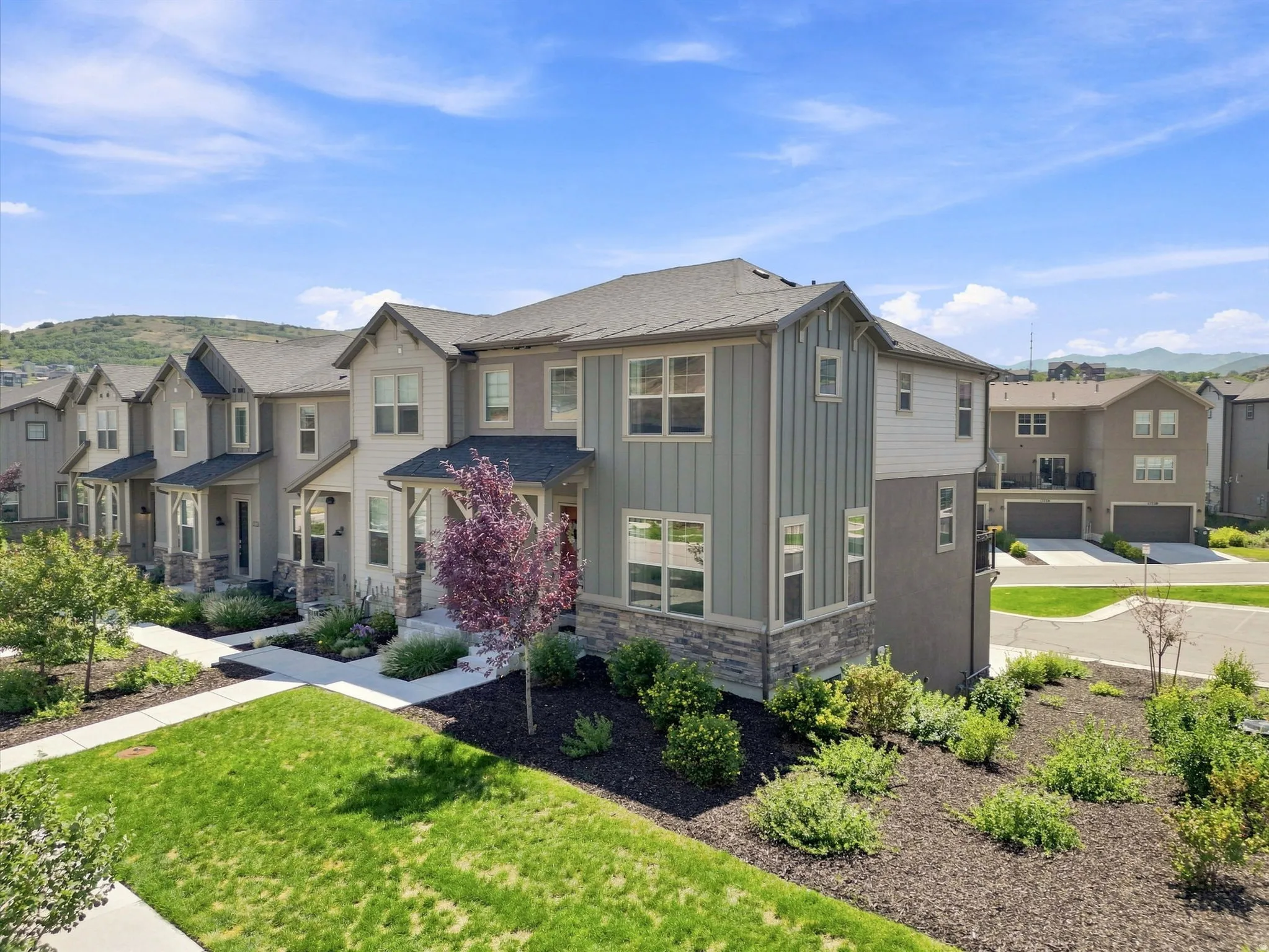 Modern townhome exterior with mixed siding and stone veneer, featuring a covered entry and landscaping with mature trees