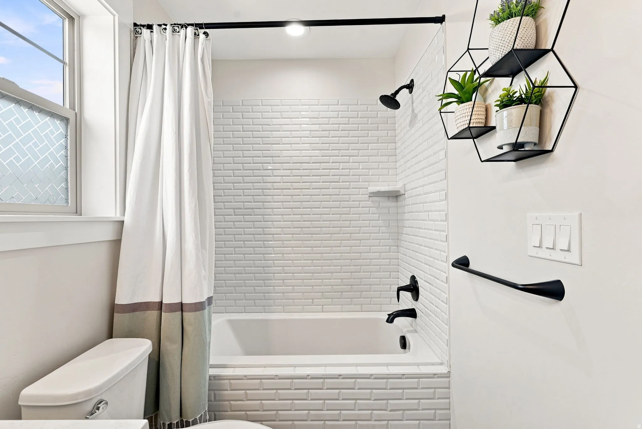Bathtub with white subway tile surround, matte black shower fixtures, and a clear glass shower screen