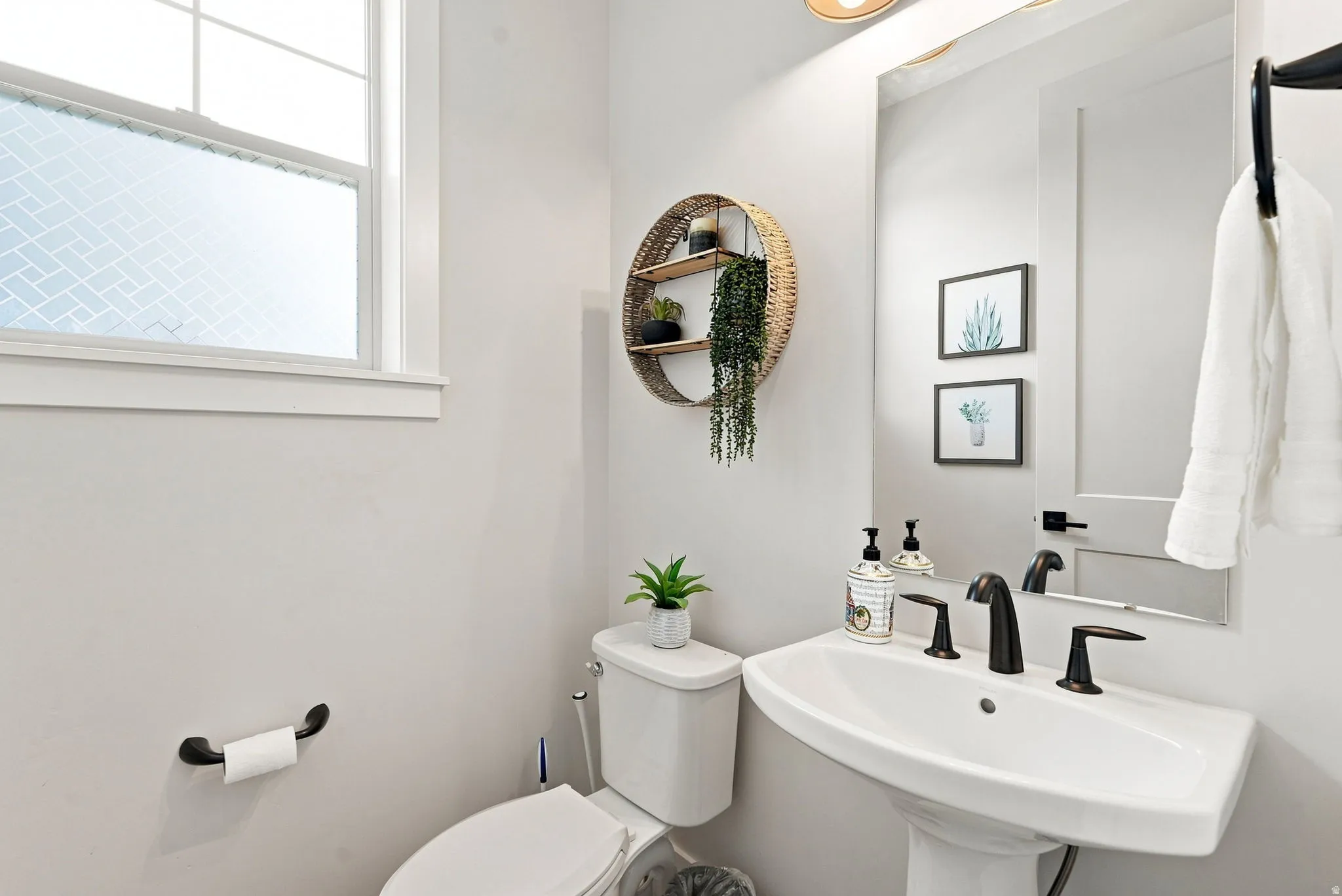 Pedestal sink with a matte black faucet, a large wall mirror, and a window with patterned privacy film