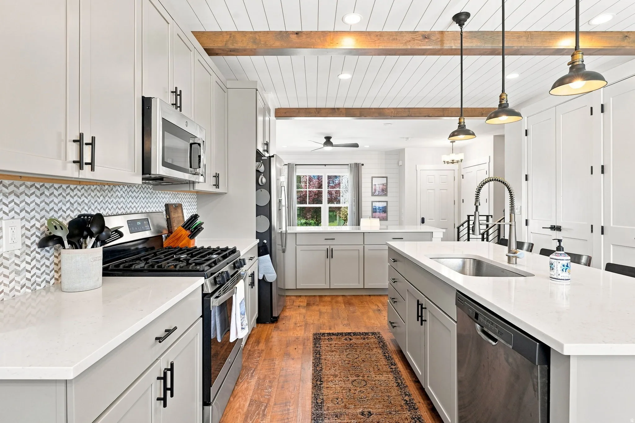 Modern kitchen featuring light gray cabinetry, stainless steel appliances, white countertops, and a herringbone tile backsplash