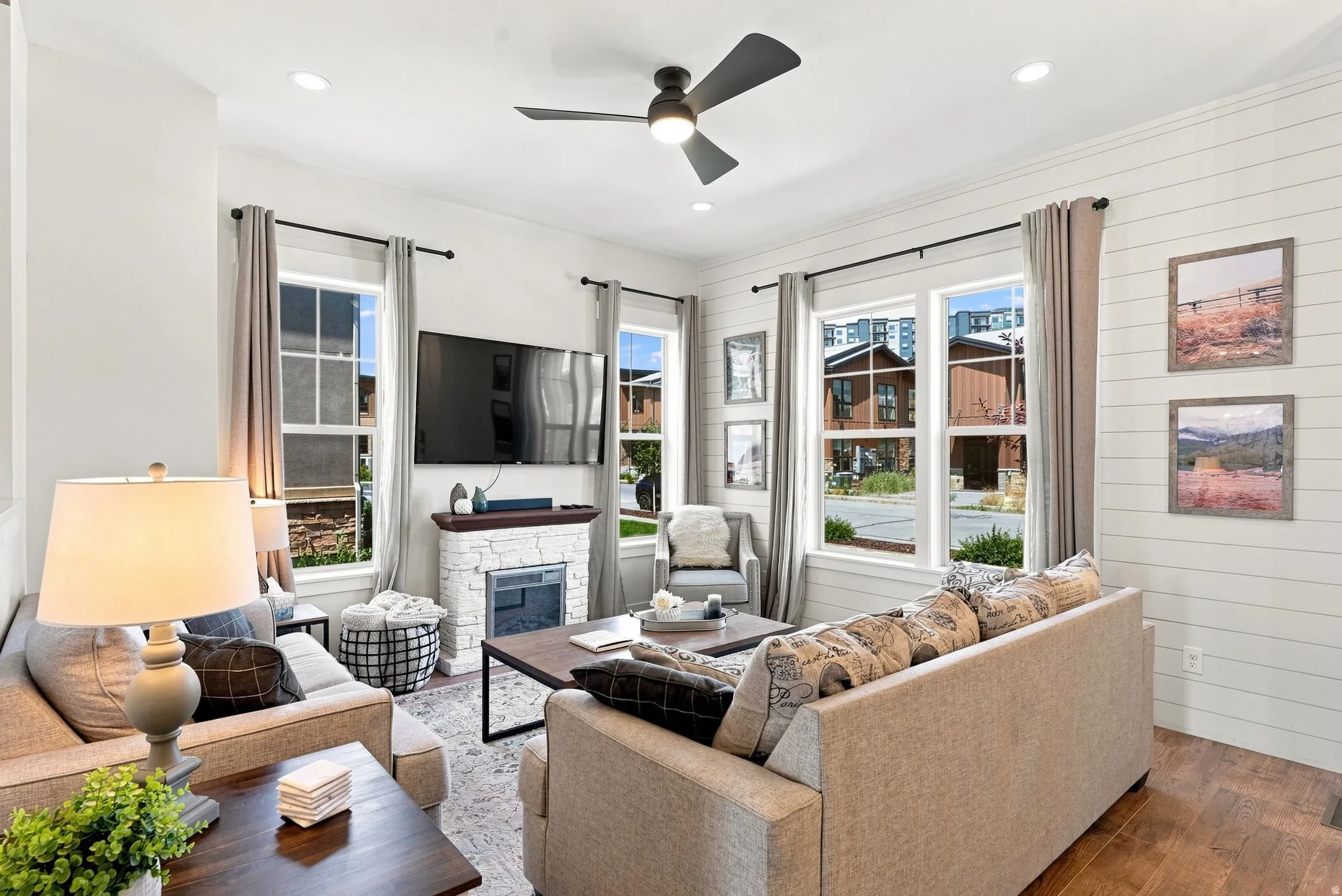 Living area featuring shiplap accent walls, wood-finish flooring, a ceiling fan with integrated lighting, and multiple windows
