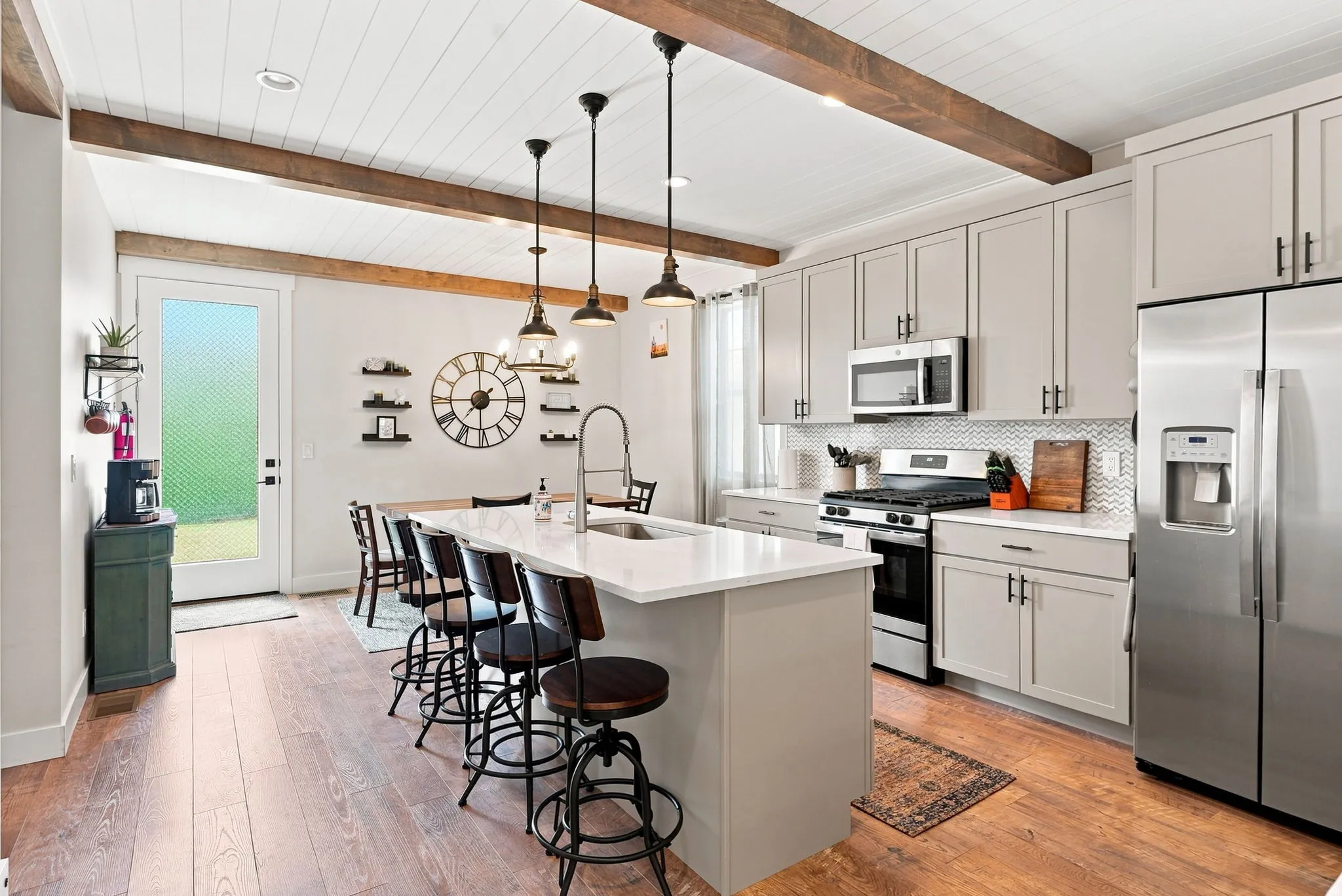 Open-concept kitchen with wood-finish flooring, a central island with seating, pendant lighting, stainless steel appliances, and ceiling beams