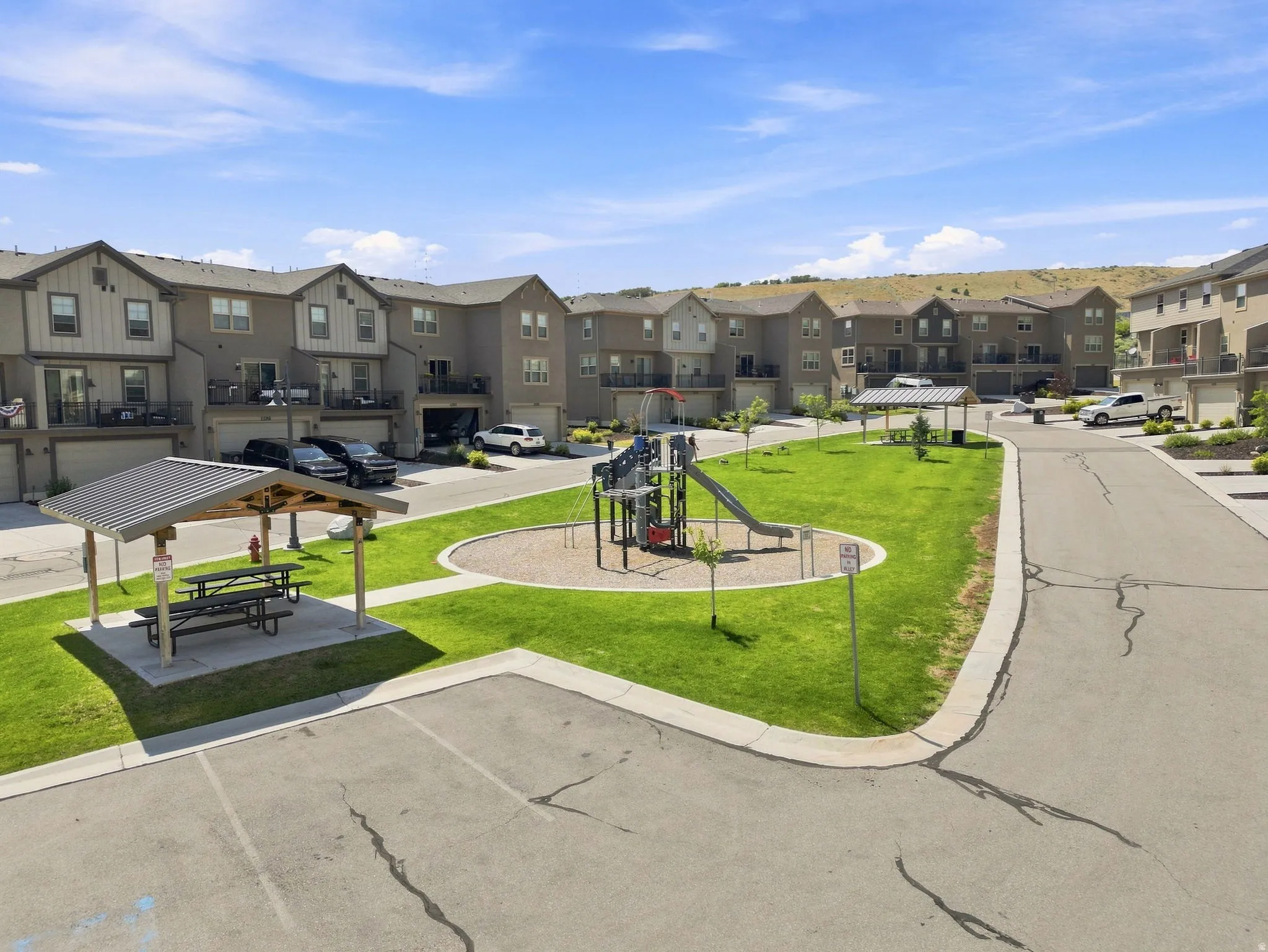 Community green space with a playground and covered picnic area, surrounded by multi-story residential buildings featuring attached garages and balconies