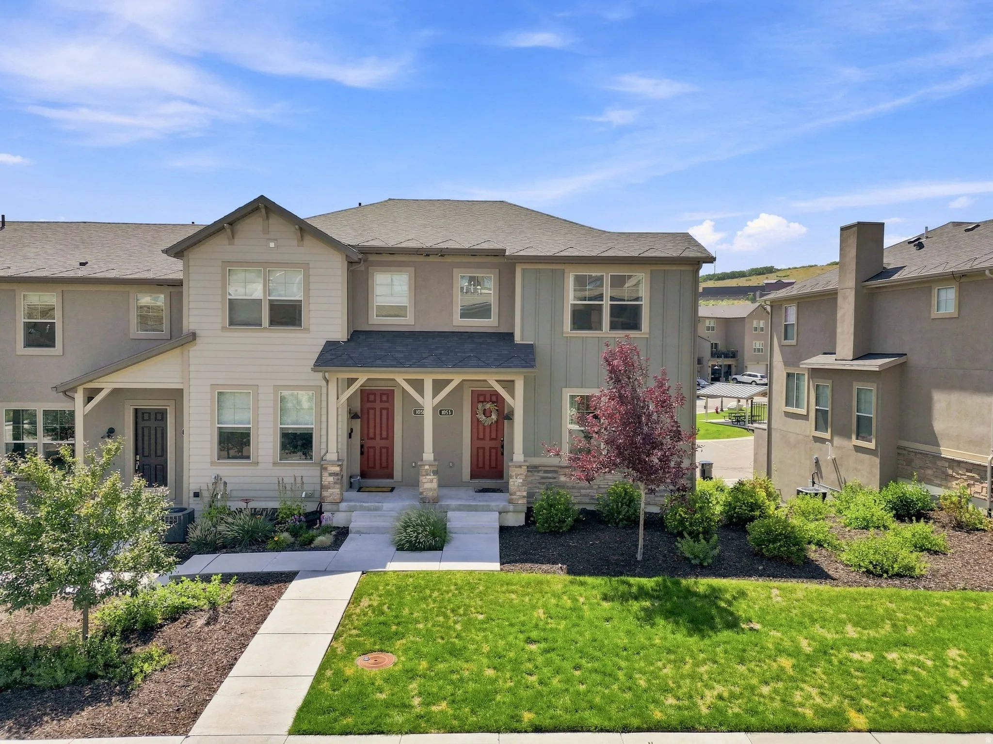 Two-story residence featuring a covered front porch with stone accents, mature landscaping, and a vibrant green lawn