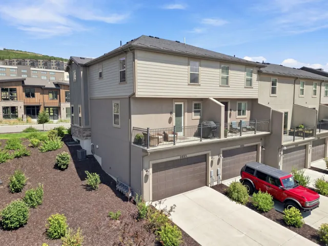 Multi-level townhouse with private balconies, attached garages, and a sloped, landscaped front yard