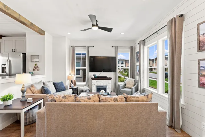 Open-concept living space featuring wood-finish flooring, a contemporary ceiling fan, and a fireplace with a white stone surround
