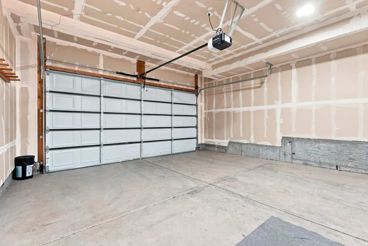 Spacious garage featuring a modern glass-panel overhead door, concrete flooring, coffered ceiling with recessed lighting, and a projector mount for enhanced functionality