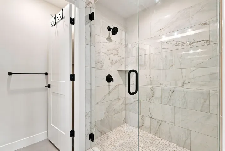 Walk-in shower with clear glass enclosure, large format wall tiles, hexagonal floor tiles, and matte black fixtures