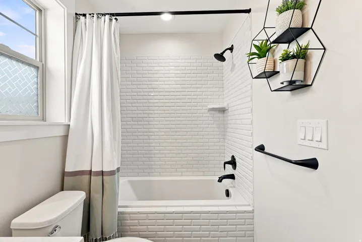 Bathtub with white subway tile surround, matte black shower fixtures, and a clear glass shower screen