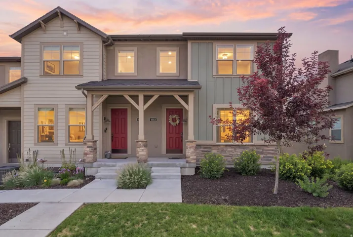 Multi-unit residence featuring two distinct red entry doors, a covered porch with stone-clad columns, and a landscaped front yard