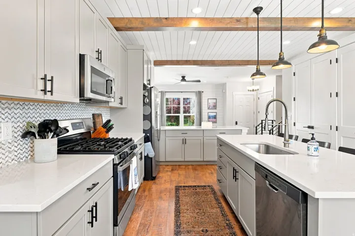 Modern kitchen featuring light gray cabinetry, stainless steel appliances, white countertops, and a herringbone tile backsplash