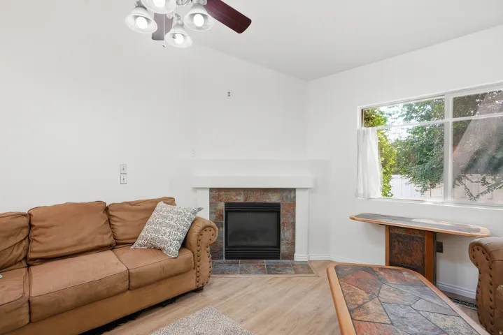 Spacious living room featuring a wood-burning fireplace with a clean-lined surround, wood-finish flooring throughout, and large windows with natural light