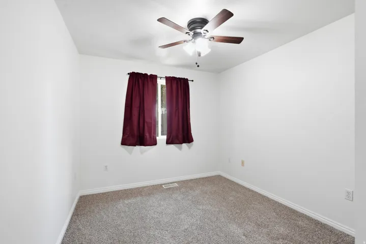 Neutral wall color, carpeted flooring, window with vertical blinds, and a ceiling fan with integrated lighting