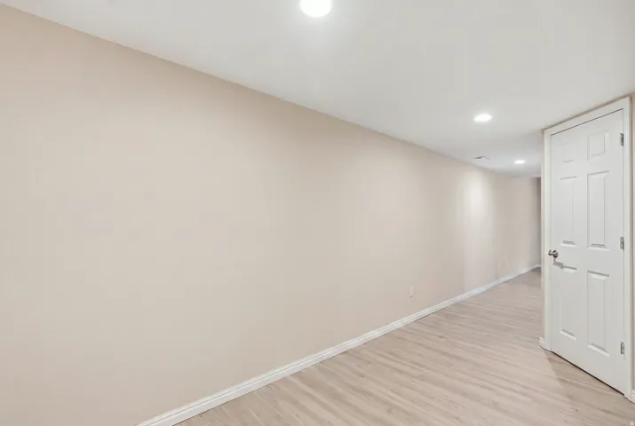 Light-toned wood-finish flooring, recessed ceiling lighting, light-colored walls, white trim, and a paneled white door