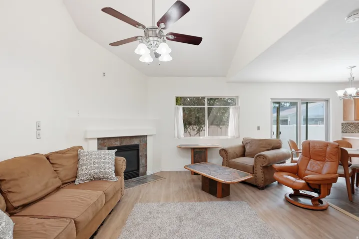 Vaulted ceiling with a ceiling fan and light fixture, fireplace with a stone surround and mantel, wood-finish flooring, and sliding glass doors