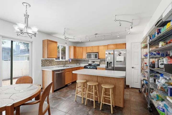 Kitchen featuring light wood cabinetry, white countertops, stainless steel appliances, a mosaic tile backsplash, and sliding glass doors