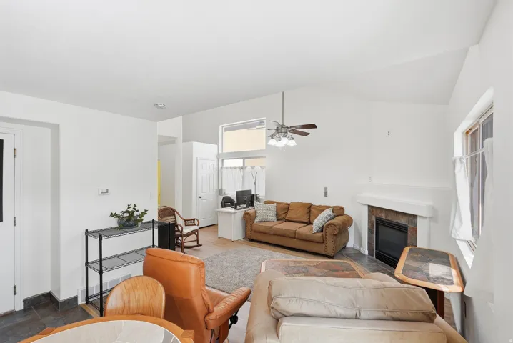 Vaulted ceiling, ceiling fan, fireplace with stone surround, tile flooring, and window