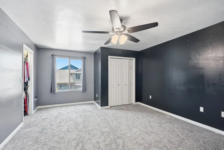 Carpeted room with a ceiling fan, a window with drapery, and bi-fold closet doors