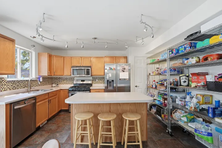 Kitchen featuring wood-finish cabinetry, stainless steel appliances, a center island with countertop seating, and track lighting
