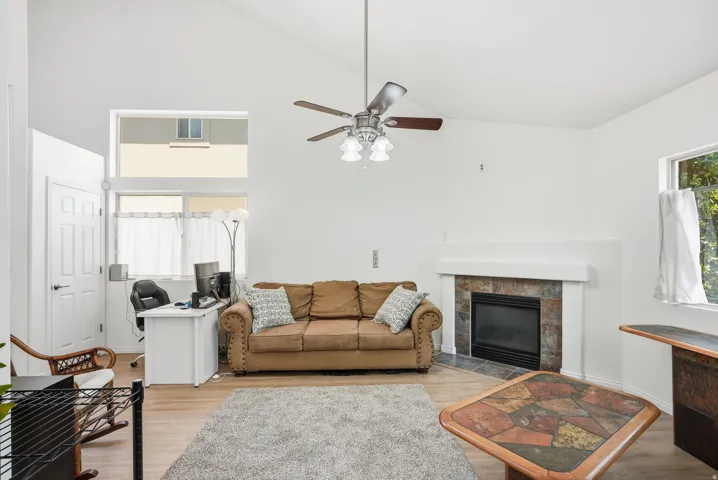 Spacious living room featuring hardwood flooring, a wood-burning fireplace with brick surround, ceiling fan with integrated lighting, and generous natural light from multiple windows