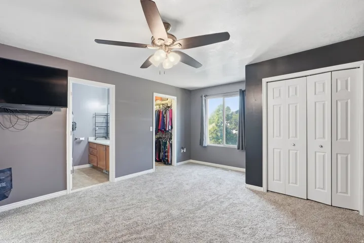 Wall-to-wall carpeting, window with outdoor scenery, ceiling fan with integrated lighting, bi-fold closet doors, and wood-finish vanity with countertop