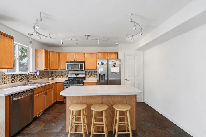 Kitchen featuring wood cabinetry, stainless steel appliances, mosaic tile backsplash, a center island with countertop, and track lighting