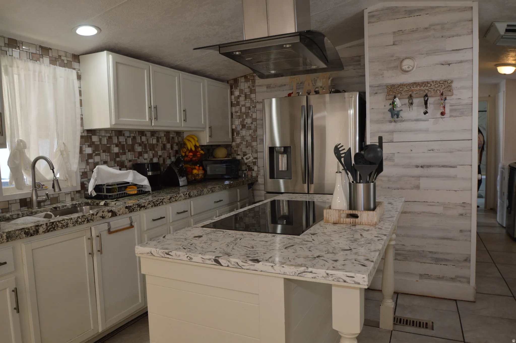 Full kitchen with white cabinetry, patterned tile backsplash, granite-finish countertops, stainless steel refrigerator, and a kitchen island with built-in cooktop