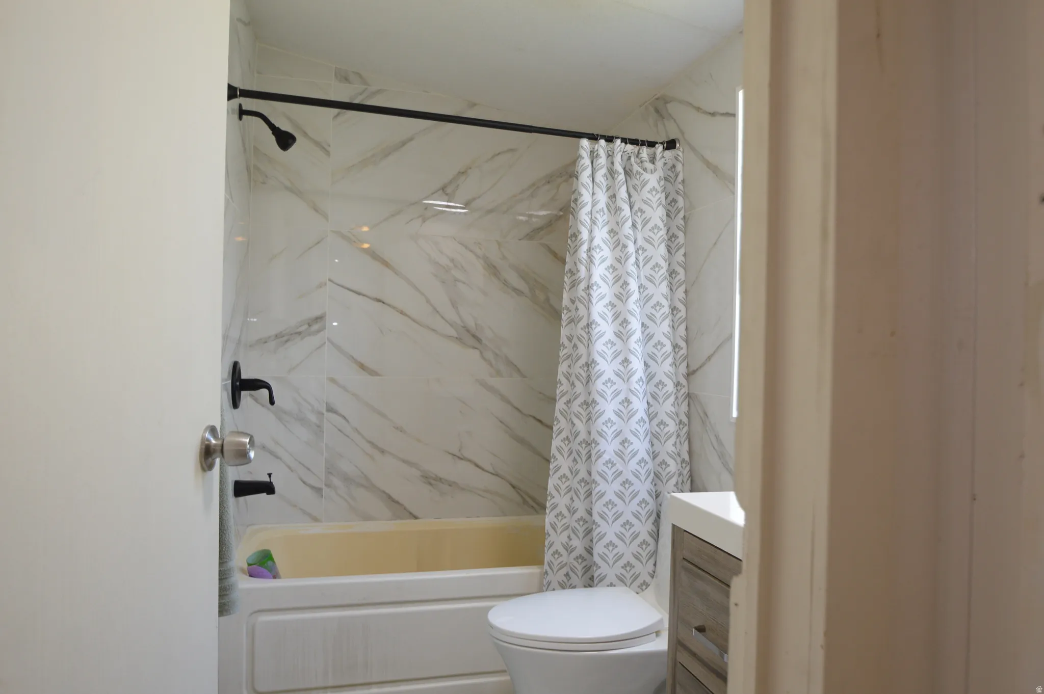 Bathtub with white subway tile surround, black-finish plumbing fixtures, and a toilet with an adjacent vanity