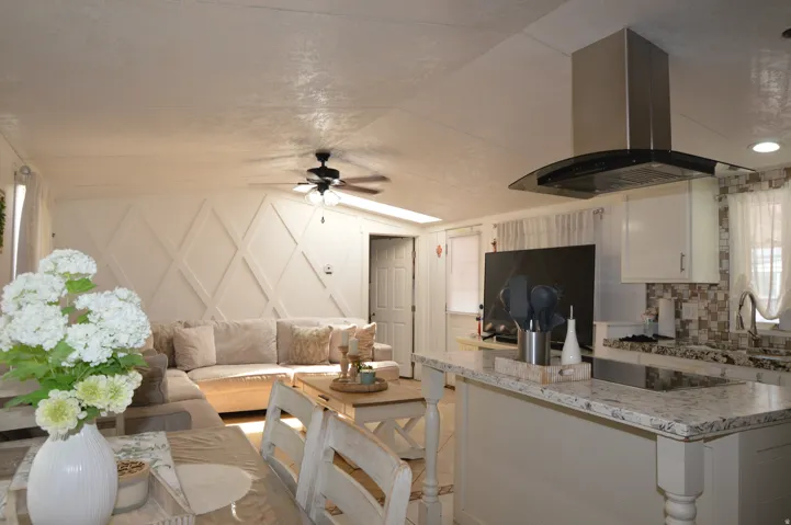 Open-concept living space featuring a geometric accent wall, ceiling fan, kitchen island with built-in cooktop, and a stainless steel range hood