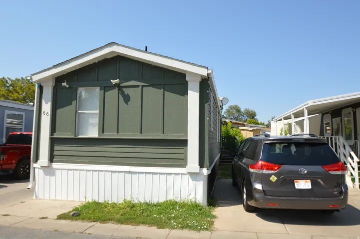 Green horizontal siding with white trim, white skirting, and a paved driveway