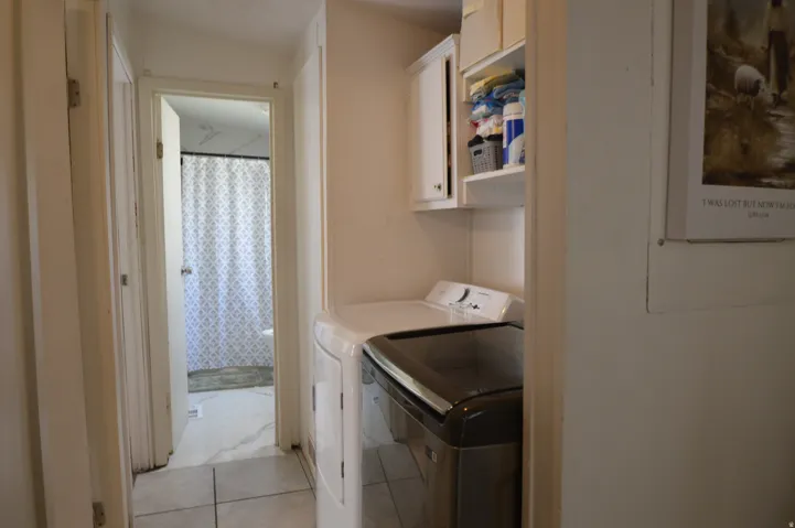 Dedicated laundry area featuring white upper cabinetry and an open shelf
