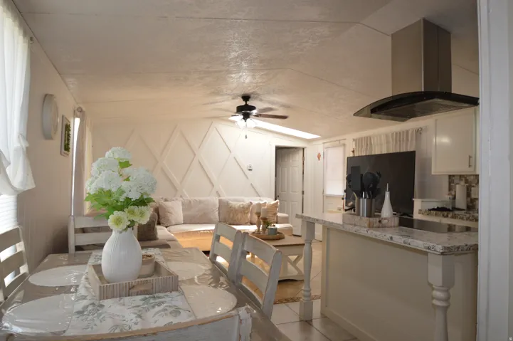 Vaulted ceiling, open-concept layout, kitchen island with solid surface countertop, stainless steel range hood, and decorative accent wall paneling
