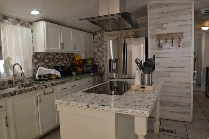 Full kitchen with white cabinetry, patterned tile backsplash, granite-finish countertops, stainless steel refrigerator, and a kitchen island with built-in cooktop