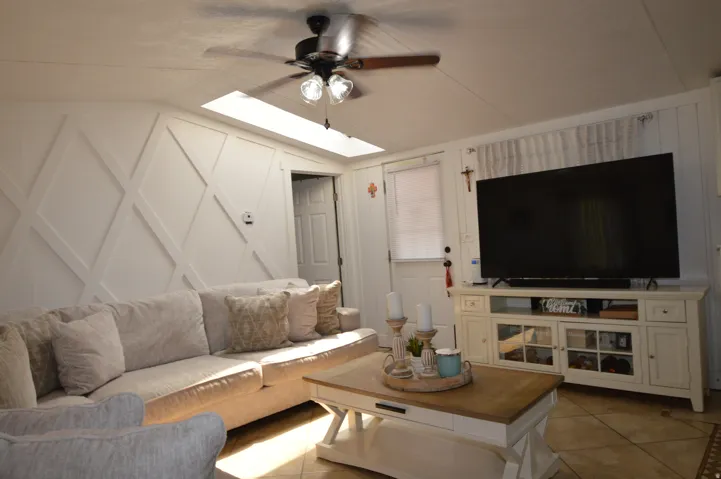 Tray ceiling with a ceiling fan, geometric wall paneling, and an overhead skylight