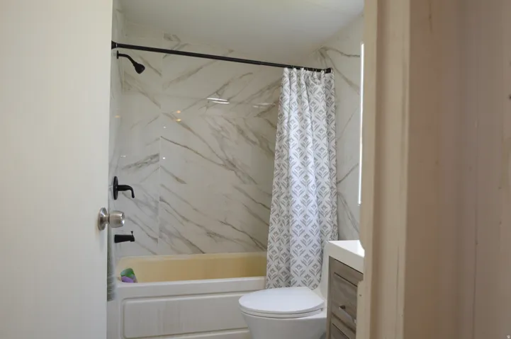 Bathtub with white subway tile surround, black-finish plumbing fixtures, and a toilet with an adjacent vanity