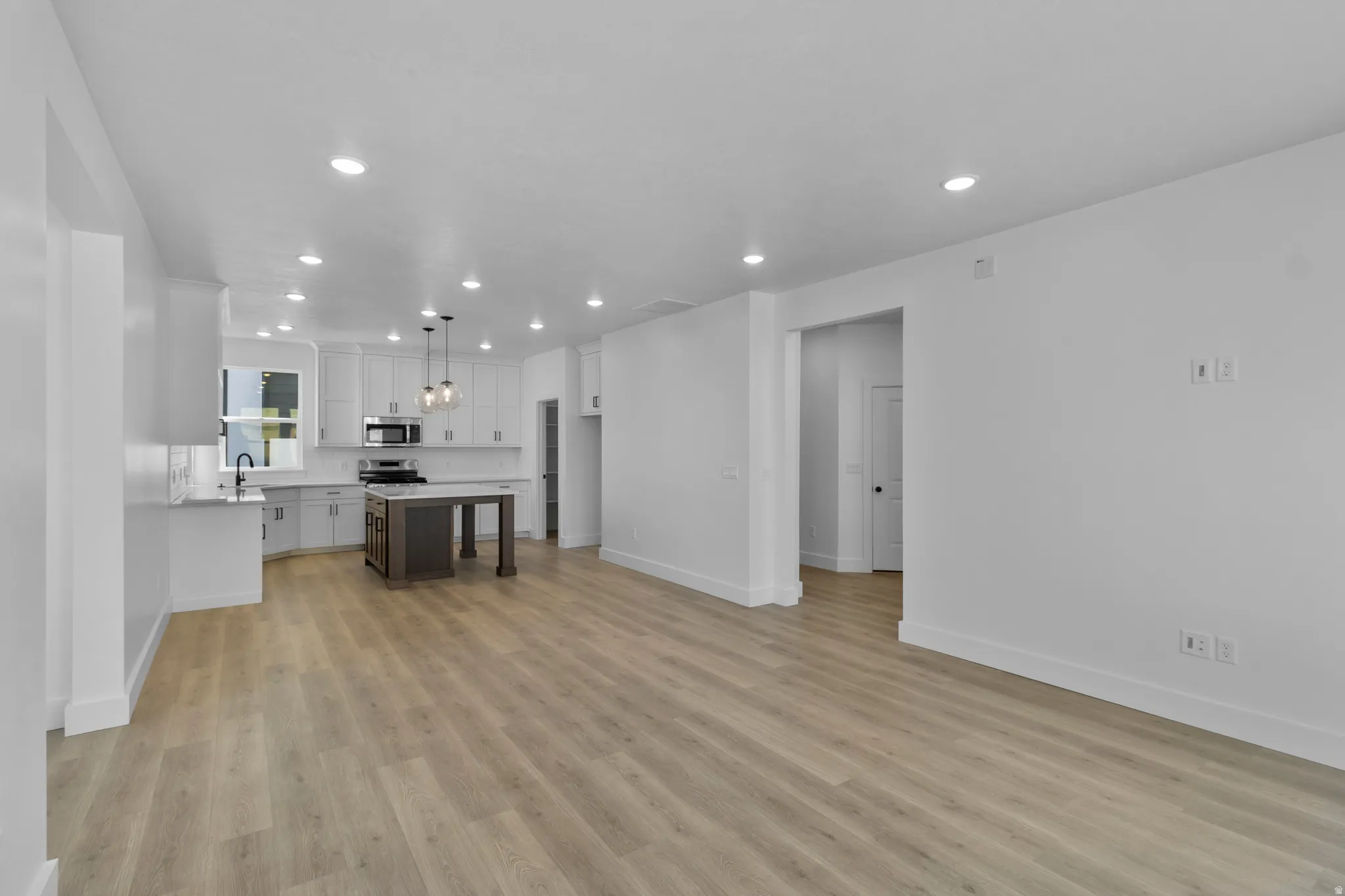 Wood-finish flooring throughout, recessed lighting, white cabinetry, dark island with light countertop, and stainless steel appliances