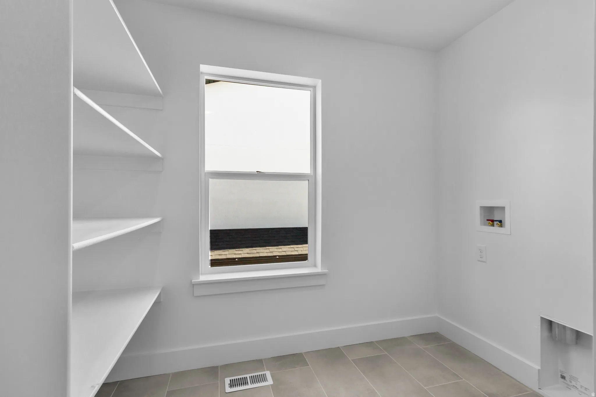 Recessed wall shelving, single window, tiled flooring, laundry hookups, and a neutral color palette