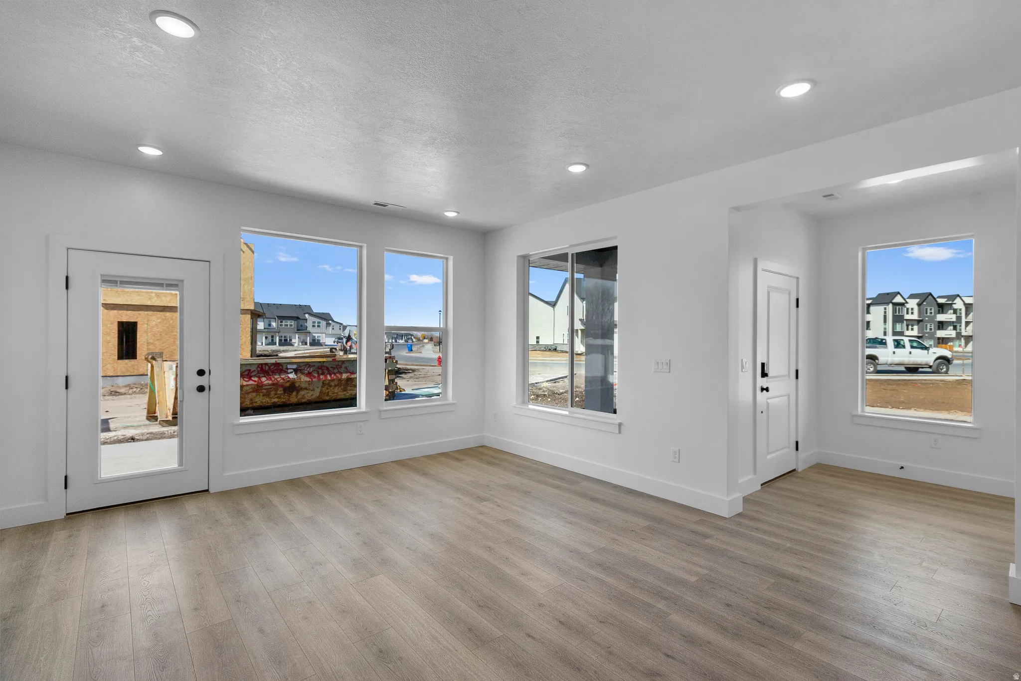 Recessed ceiling lighting, durable wood-finish flooring, white walls, multiple windows, and a glass-paneled exterior door
