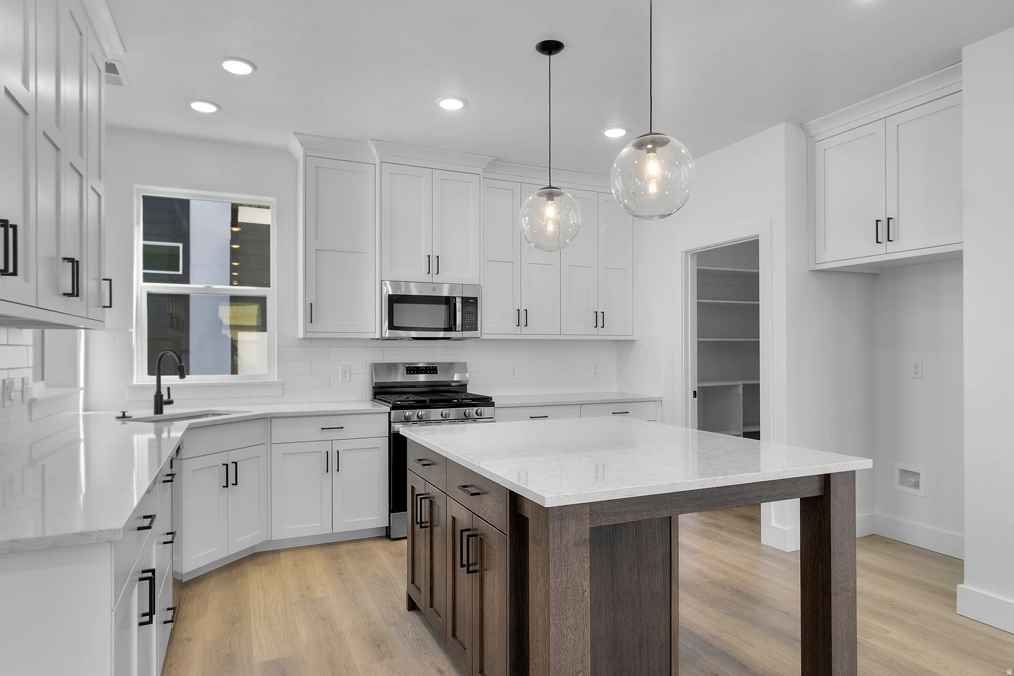 Modern kitchen featuring white shaker cabinetry, stainless steel appliances, a center island with a stone countertop, wood-finish flooring, and recessed lighting