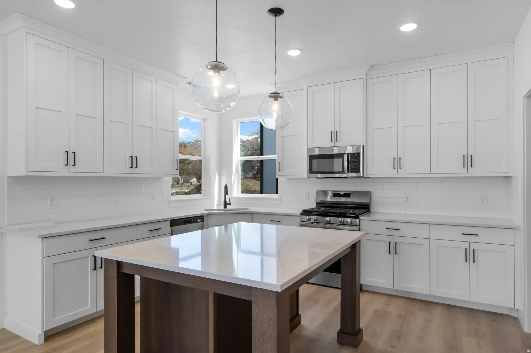 Modern kitchen featuring white shaker cabinetry, stainless steel appliances, a large center island with a light-toned countertop, and wood-finish flooring