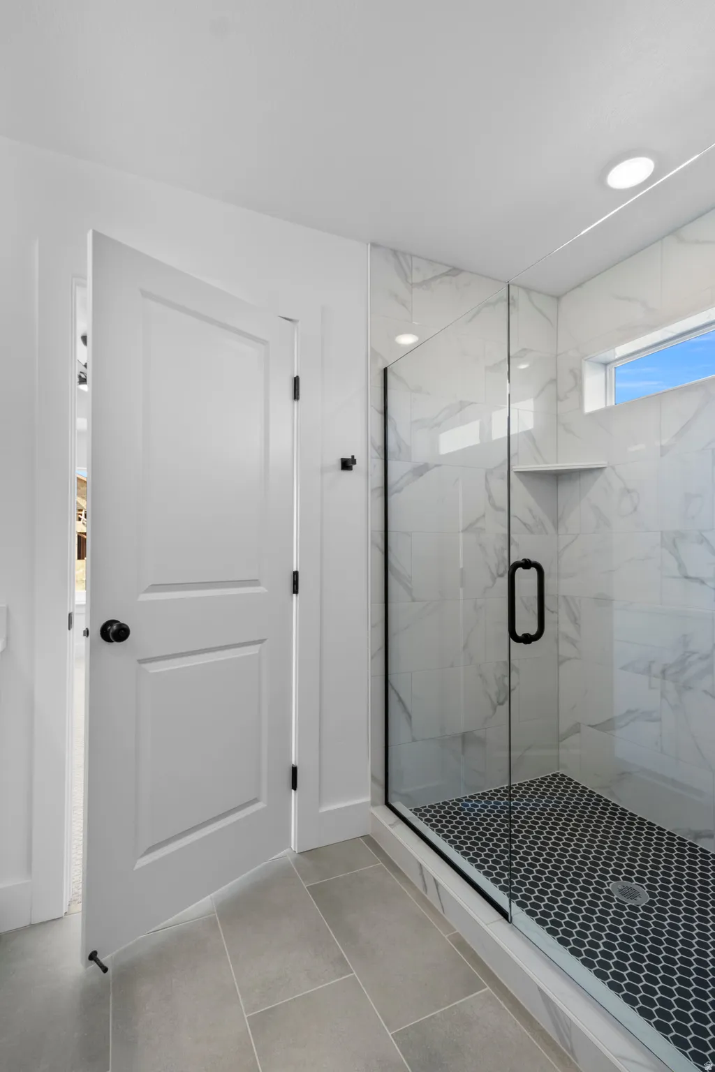 Frameless glass shower with black hardware, white marbled tile surround, built-in shower niche, and a black hex-tile shower floor