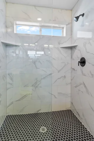 Walk-in shower with full height white tile walls, black hexagonal mosaic tile flooring, built-in shelving, and a transom window